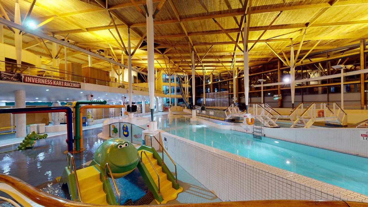 A leisure pool with a children’s slide shaped like an animal and various shallow water play features.