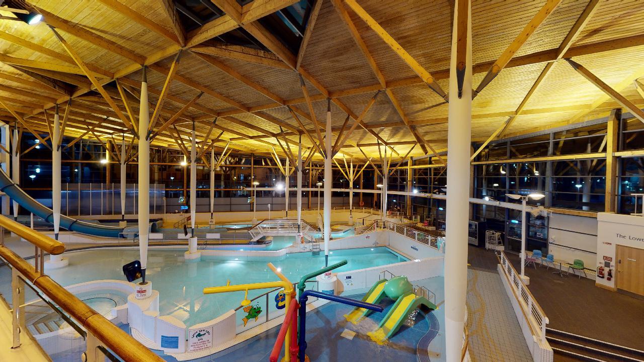 An elevated view of a leisure pool with water play equipment, small slides, and surrounding walkways.