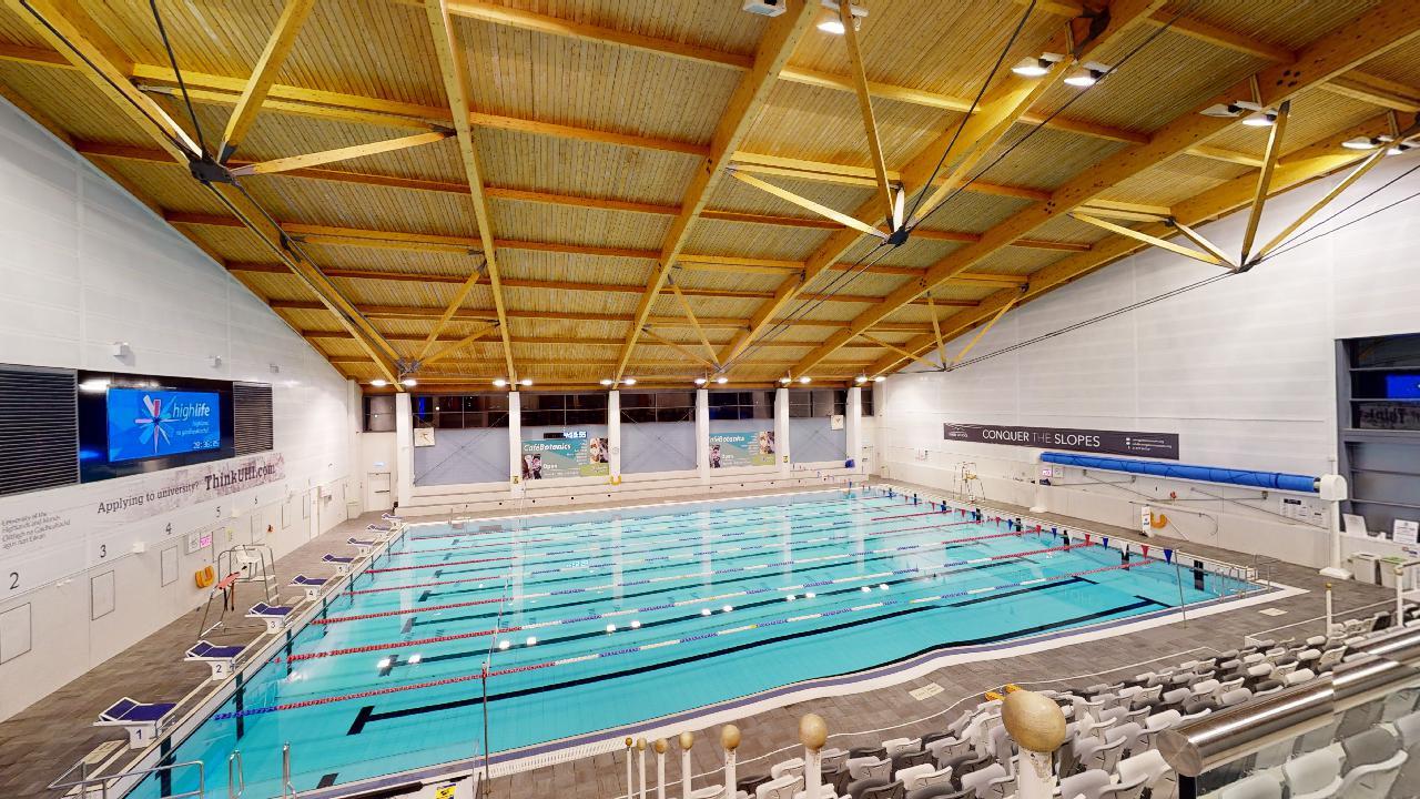 A wide view of an indoor competition pool with marked swimming lanes and surrounding spectator seating.