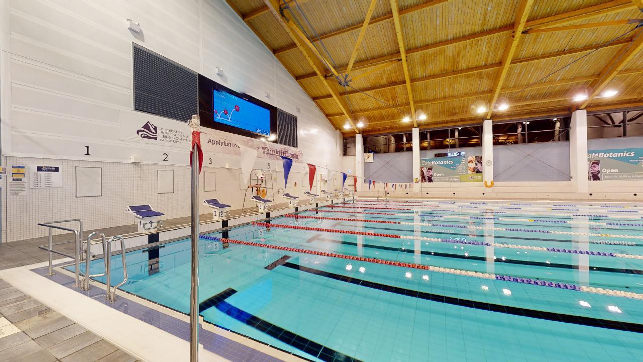 A close view of swimming lanes in an indoor pool, with lane markers and starting blocks along the pool edge.