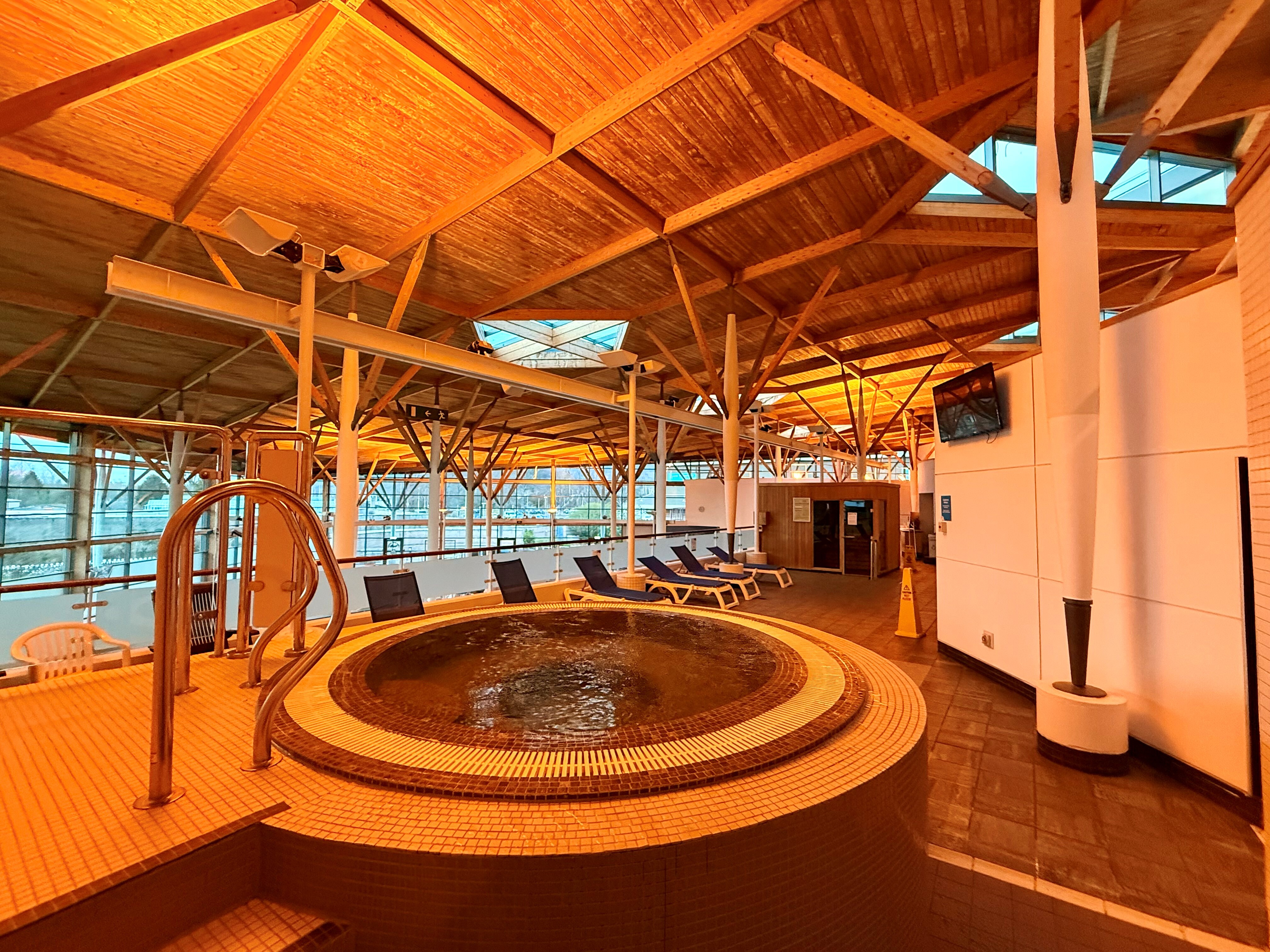 Jacuzzi bath with hand rails to assist entry into bath and relaxing sun beds behind the bath.