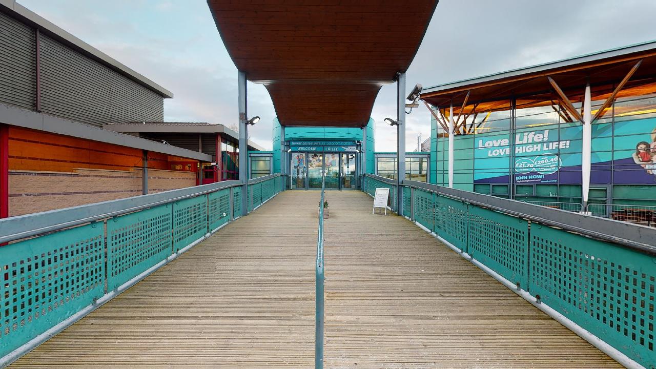 Outdoor walkway leading to a building entrance with teal railings and “Love Life! Love High Life!” signage.