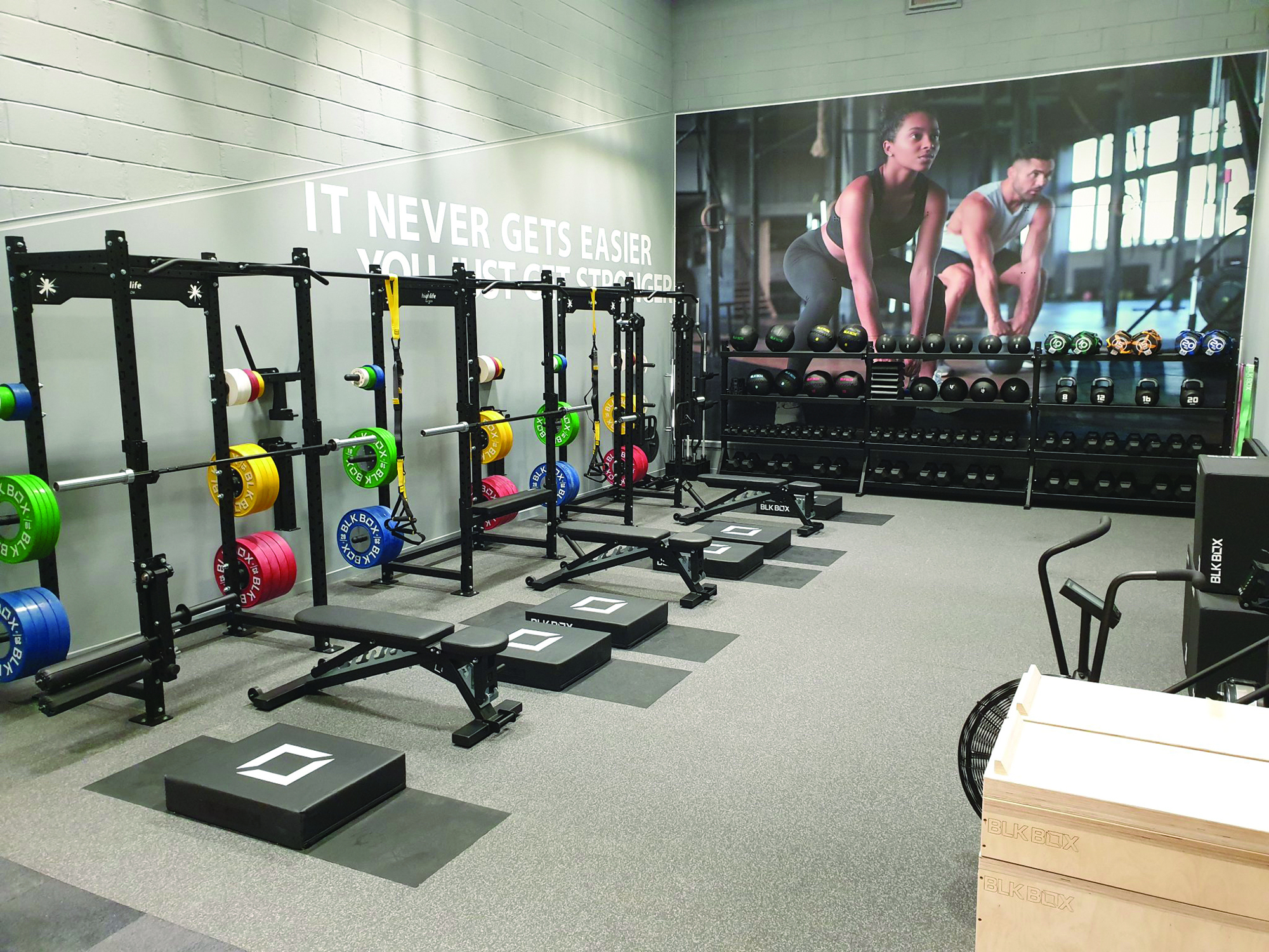 Modern gym with weightlifting racks, benches, colorful weight plates, and exercise machines in a clean, organised space.