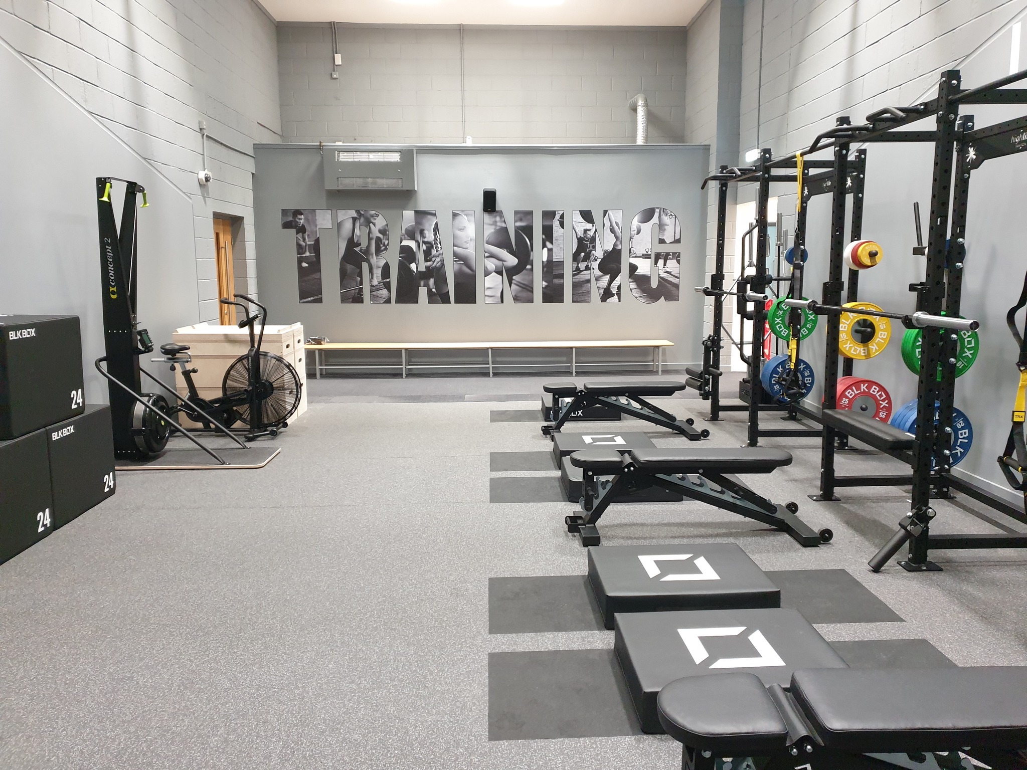 Modern gym with weightlifting racks, benches, colorful weight plates, and exercise machines in a clean, organised space.