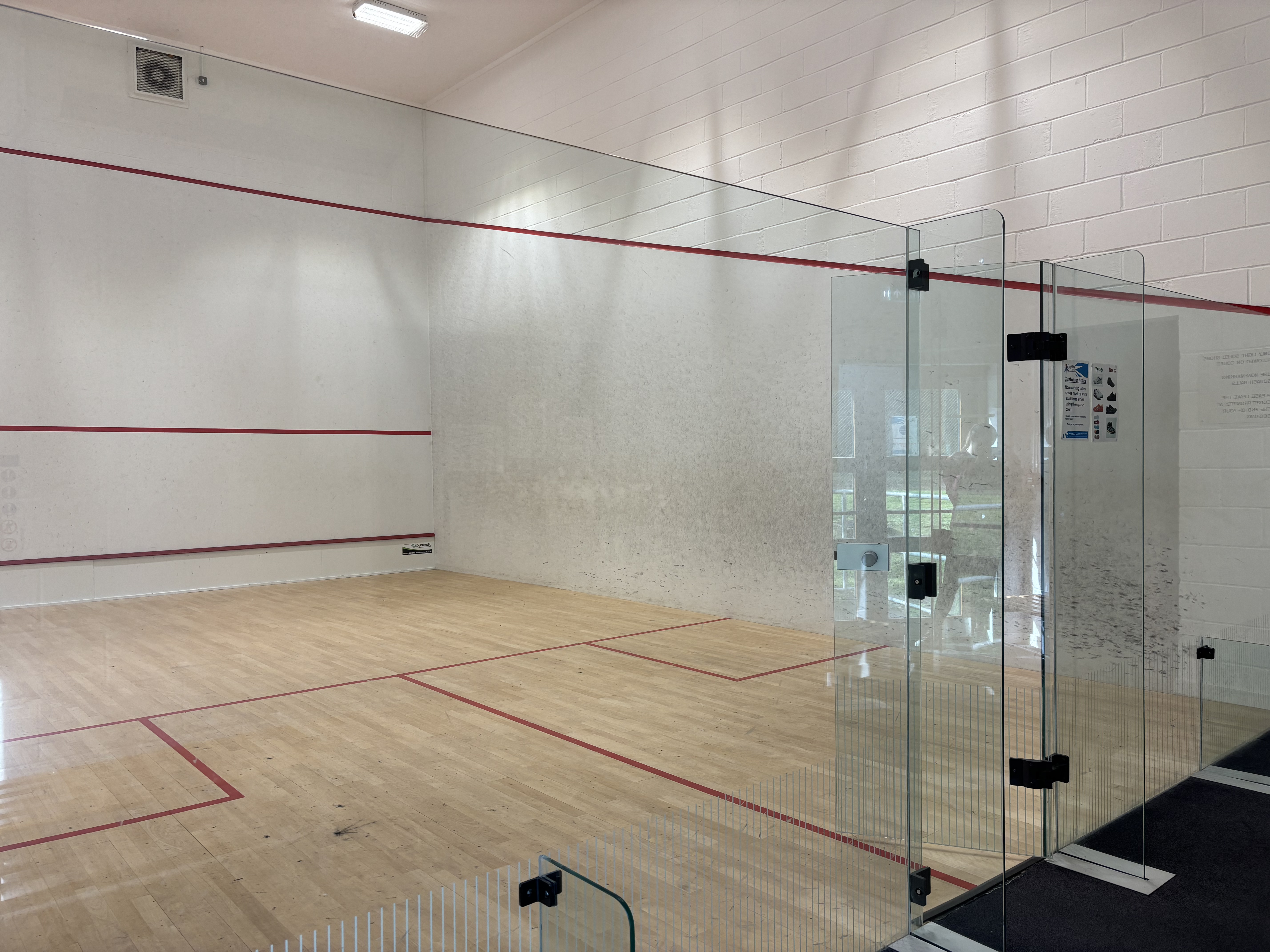 Squash court with glass wall and door opening.