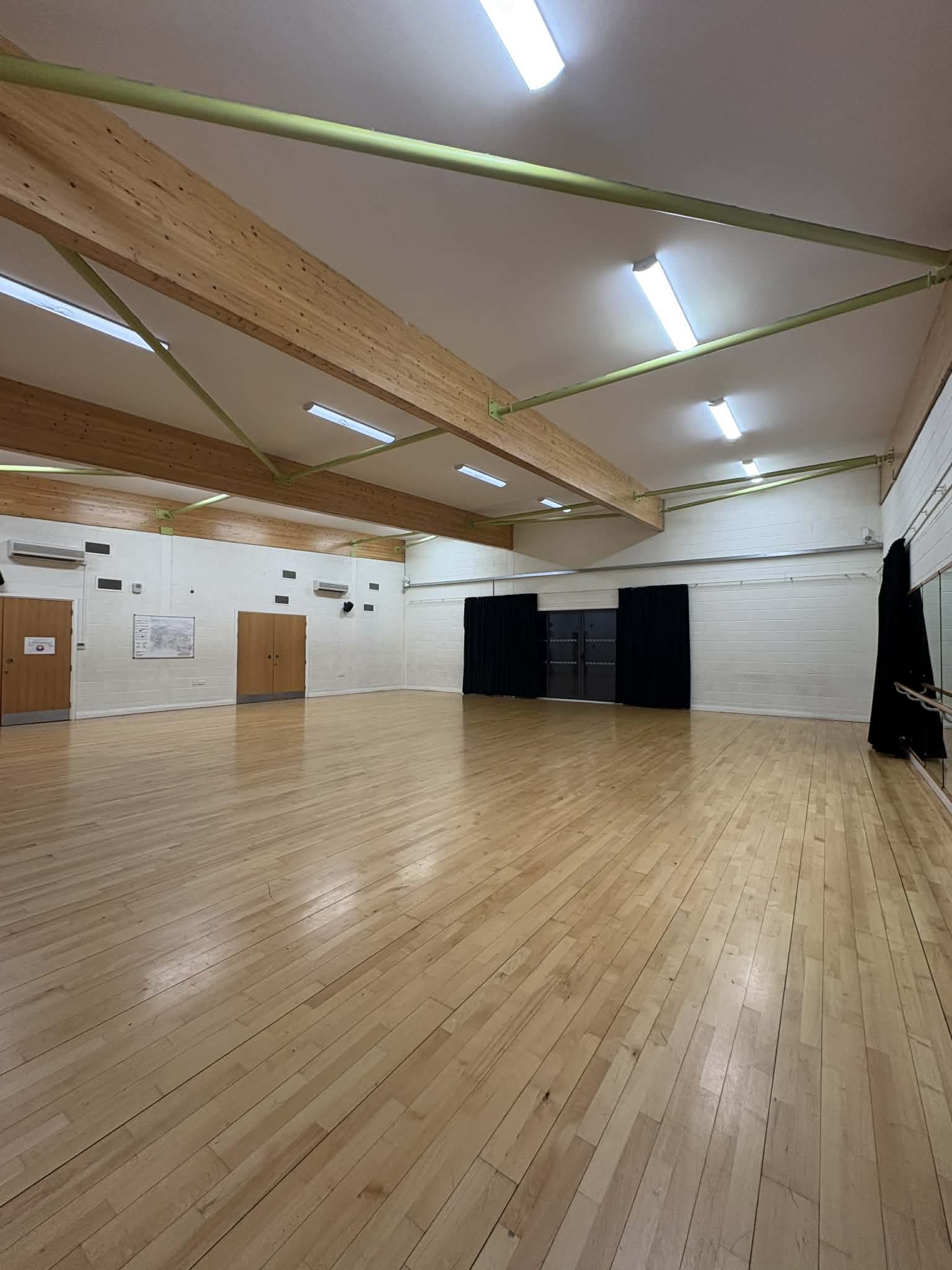 A bright and spacious dance studio with wooden flooring and a mirrored wall with a barre.