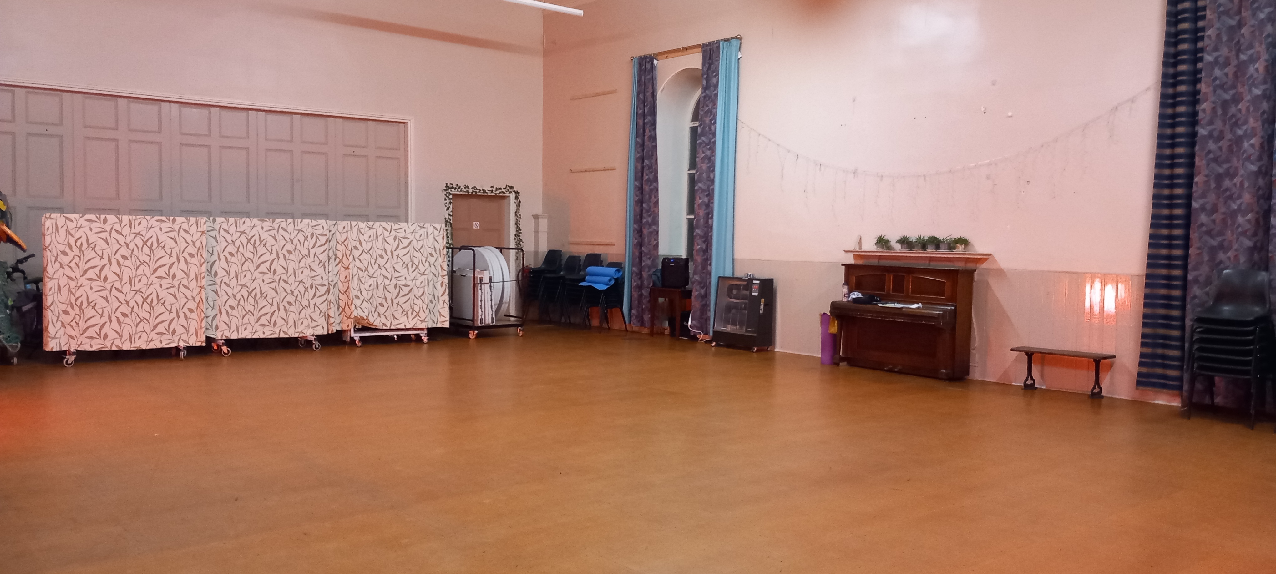 Spacious hall featuring wooden flooring and large windows, with a piano beside the wall.