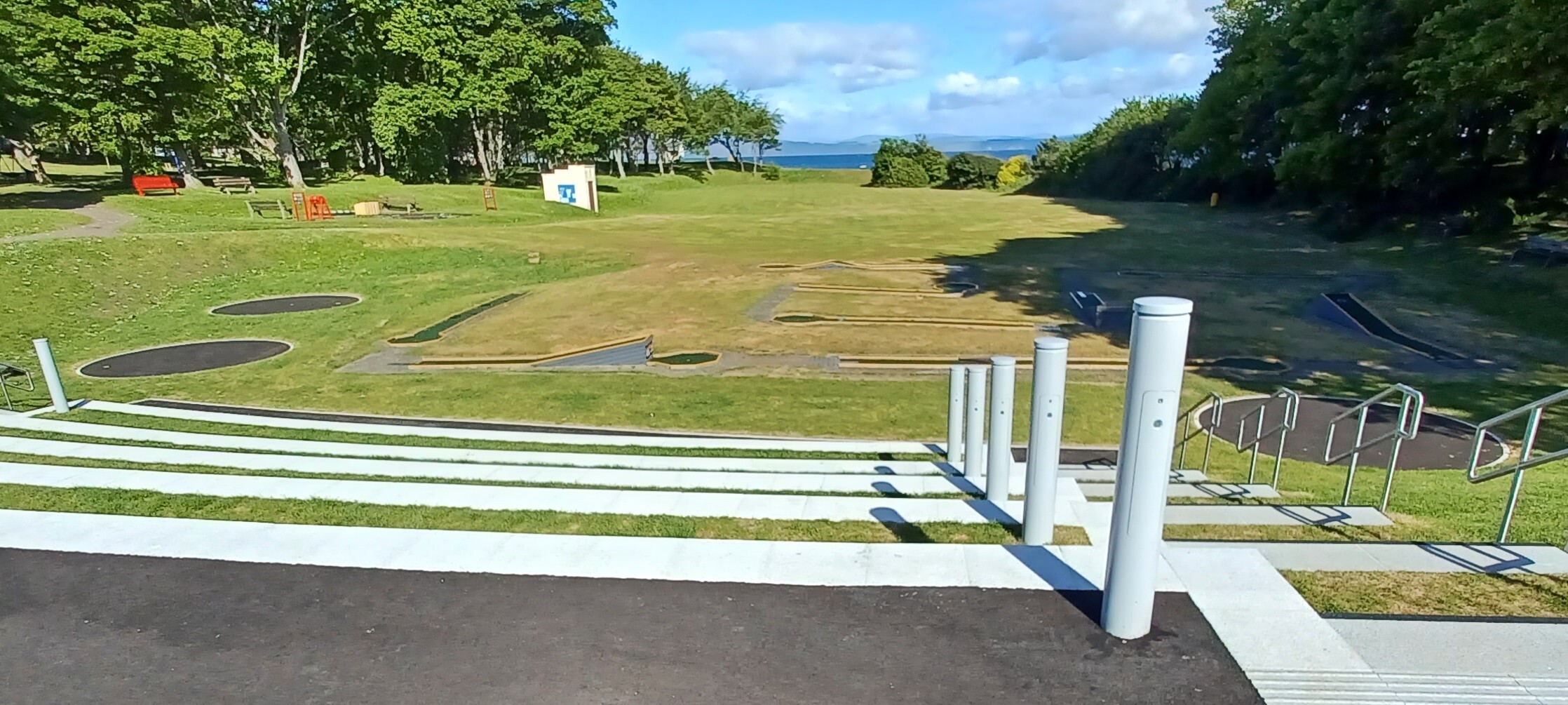 Outdoor leisure park featuring steps down to a golf putting green and the sea in the background.