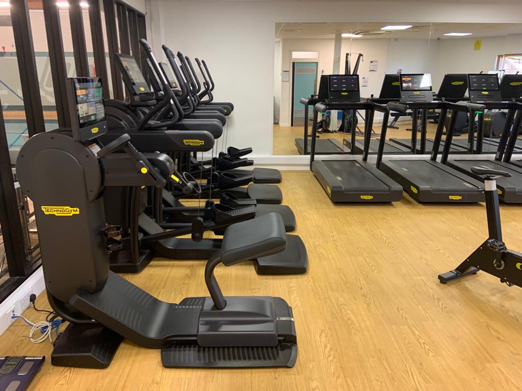 Gym with treadmills and strength equipment against mirrored walls.
