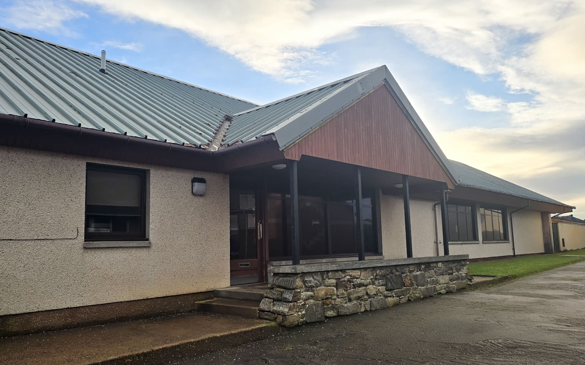 A contemporary structure with a central entrance, which boasts a covered porch adorned with a V-shaped roof and a prominent stone facade at the front.