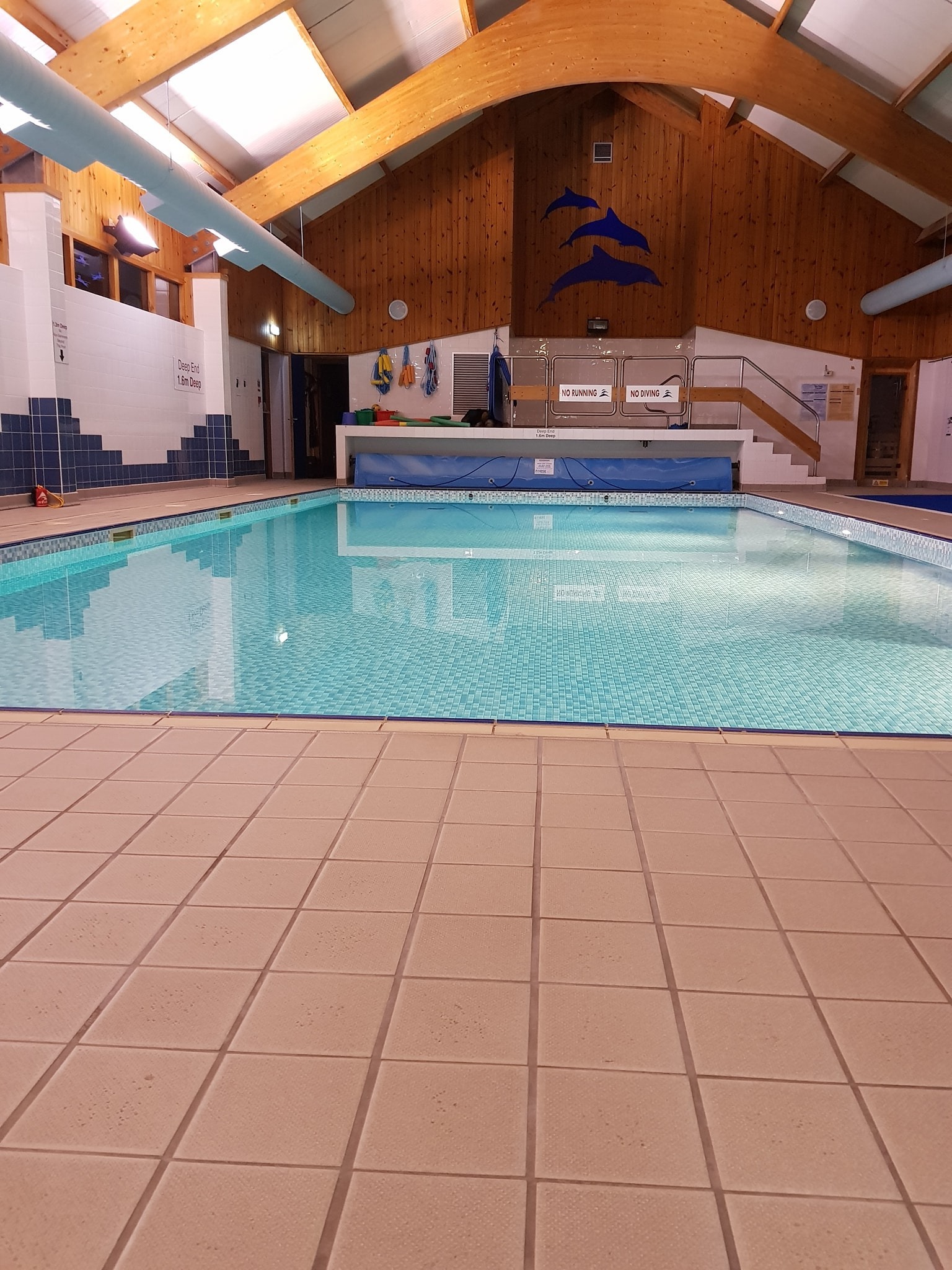 Indoor swimming pool with clear blue water, tiled flooring and walls, and bright lighting.