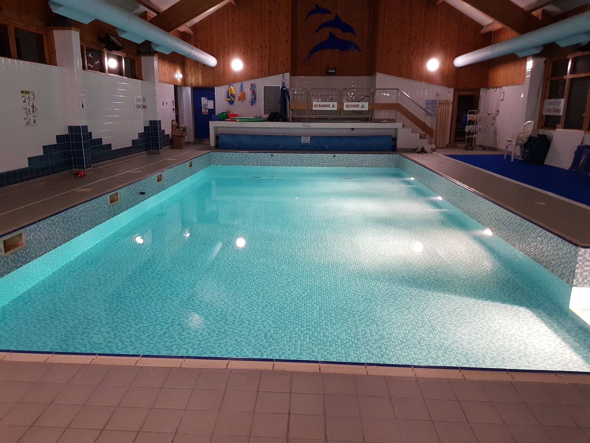 Indoor swimming pool with clear blue water, tiled flooring and walls, and bright lighting.
