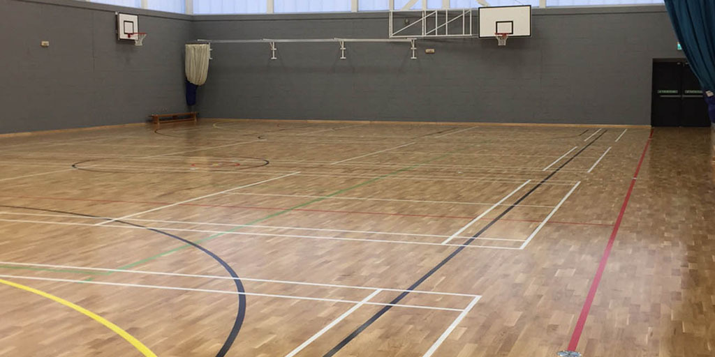 A sports hall with court lines for various sports and basketball hoops on the walls.