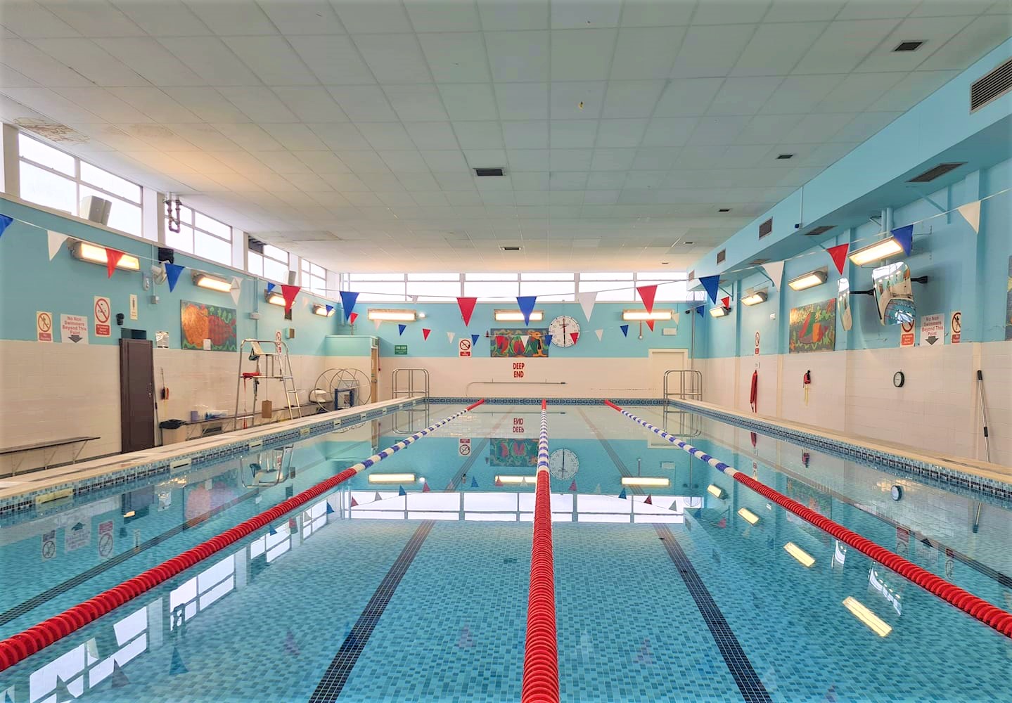 Indoor swimming pool with lane markers and colourful flags hanging above tiled walls.