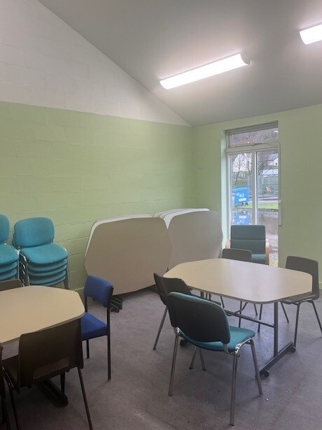 Well-lit room equipped with meeting room tables with surrounding chairs.
