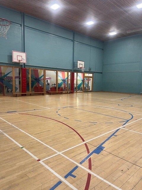 Games hall with basketball and badminton court floor markings and basketball hoop on the walls.