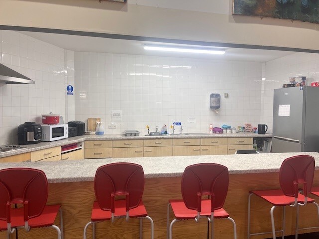 Kitchen with chairs along the front counter and featuring a hob with extraction fan, microwave, kettle and a fridge/feezer against the wall.