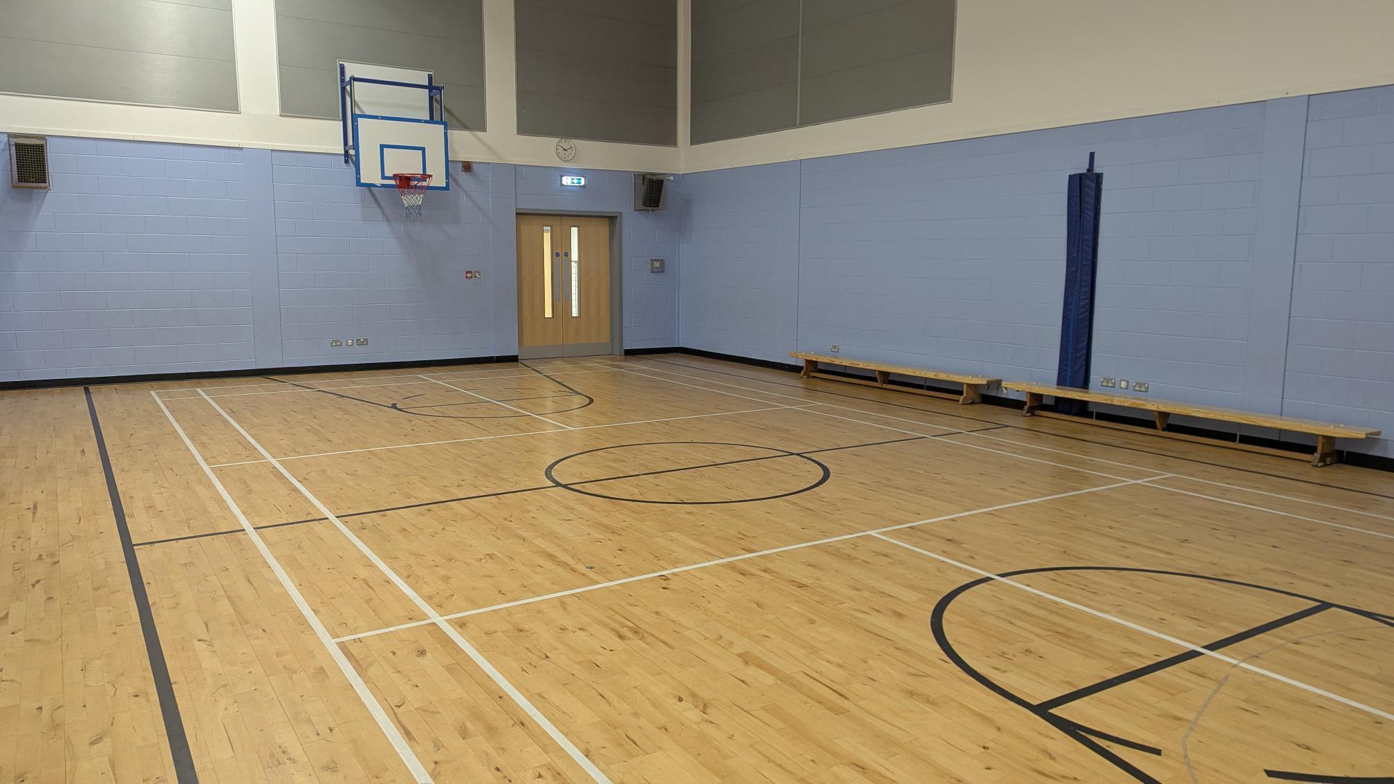 Games hall with basketball and badminton court floor markings and a basketball hoop on the wall.