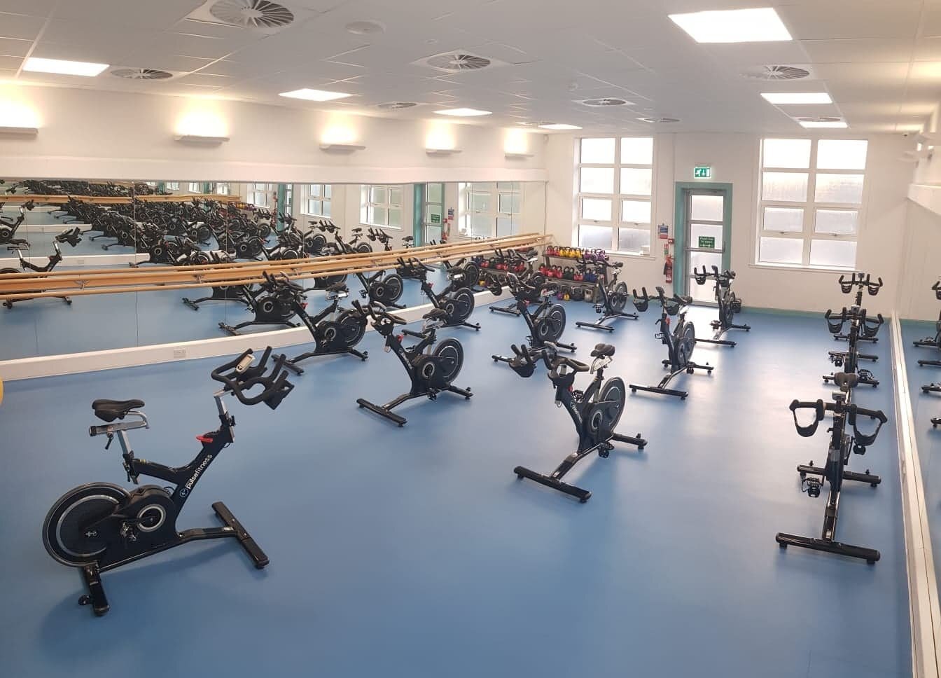 A fitness studio featuring a mirrored wall and equipped for an indoor cycling class.
