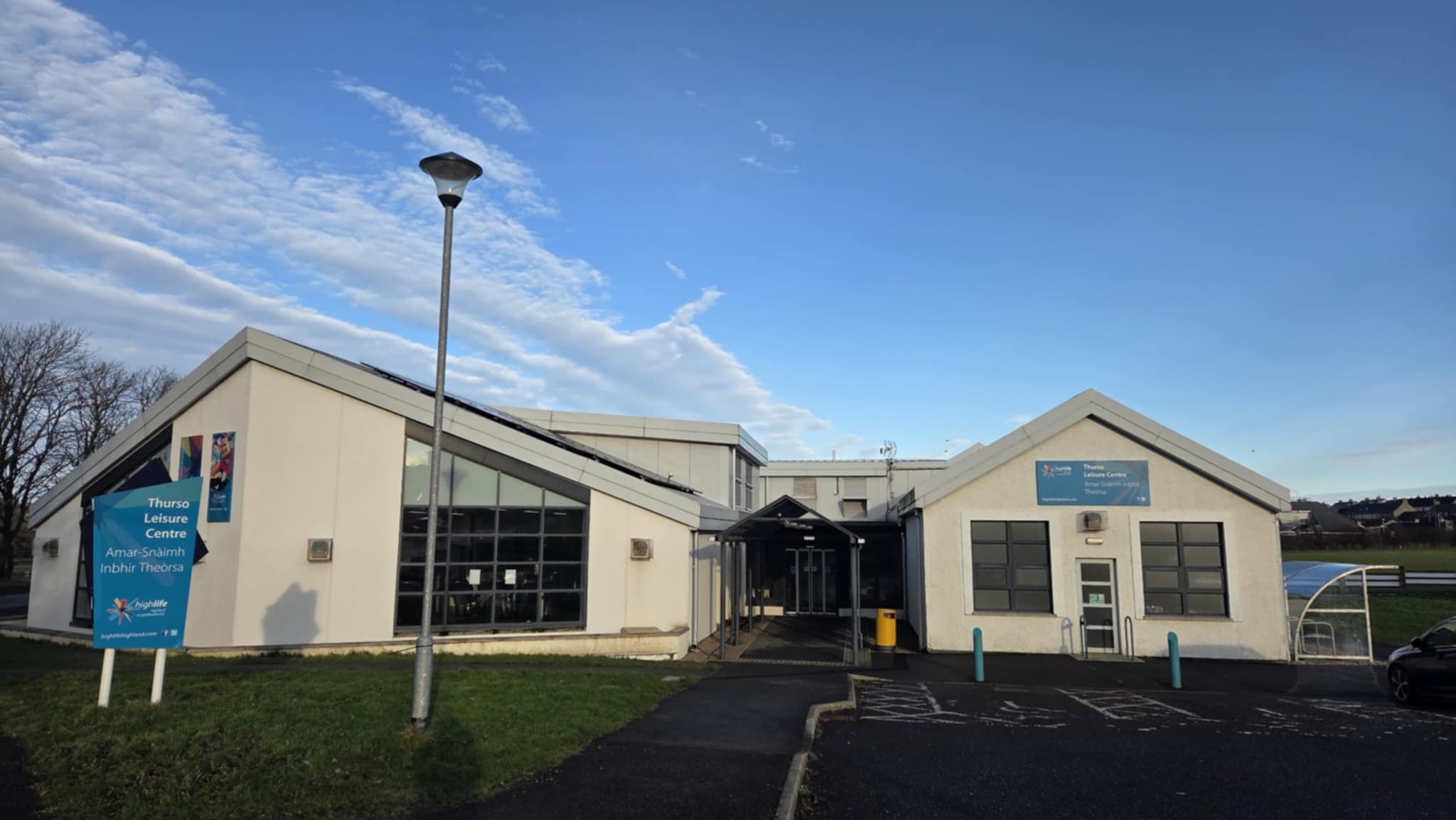 The structure is a white building featuring two sections, with a centrally located entrance. Floor-to-ceiling windows adorn the front of the main section.