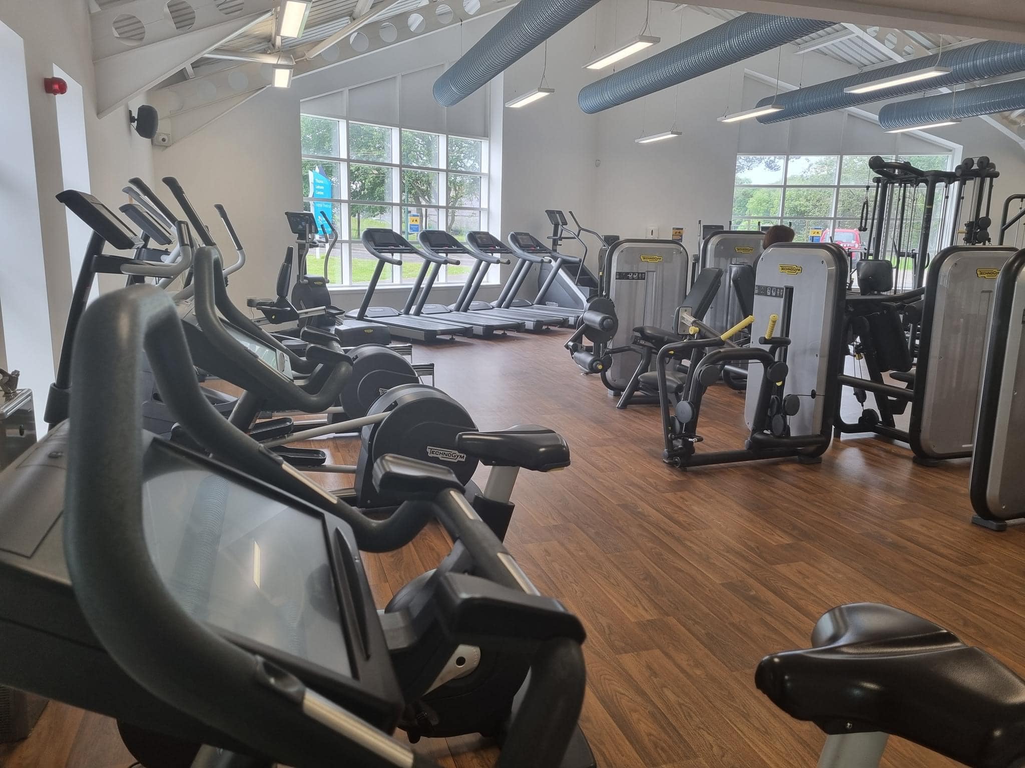Gym with treadmills and elliptical machines facing large windows with natural light.