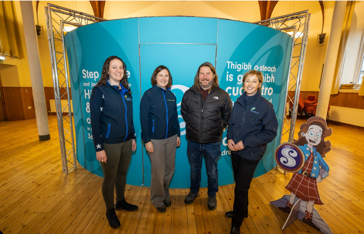 Inside a community hall space with 4 people gathered next to a small cartoon cardboard cutout.