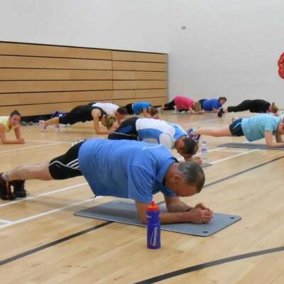 A group of people holding a plank position on exercise mats in a sports hall.