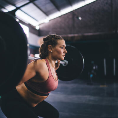 A person performing a back squat in a gym, holding a loaded barbell across their shoulders.