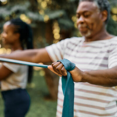 People exercising outdoors using long resistance bands, stretching them out in front of their bodies.