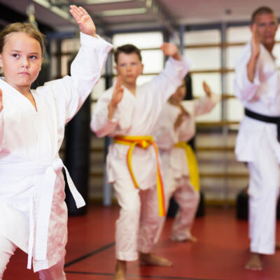 A person wearing a white martial arts uniform sitting on a wooden bench and holding a white belt loosely in their hand.