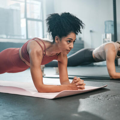 Two people hold a plank position on exercise mats in a gym, focusing on core strength during a workout session.