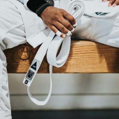 People practising Brazilian jiu‑jitsu in a bright training studio, with two individuals grappling on the mats while others train in the background.