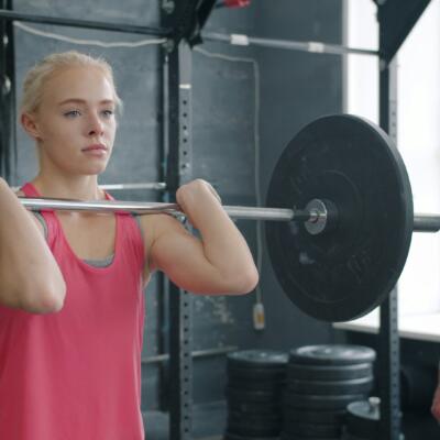 A person lifting a barbell in a gym while another person stands nearby providing support.